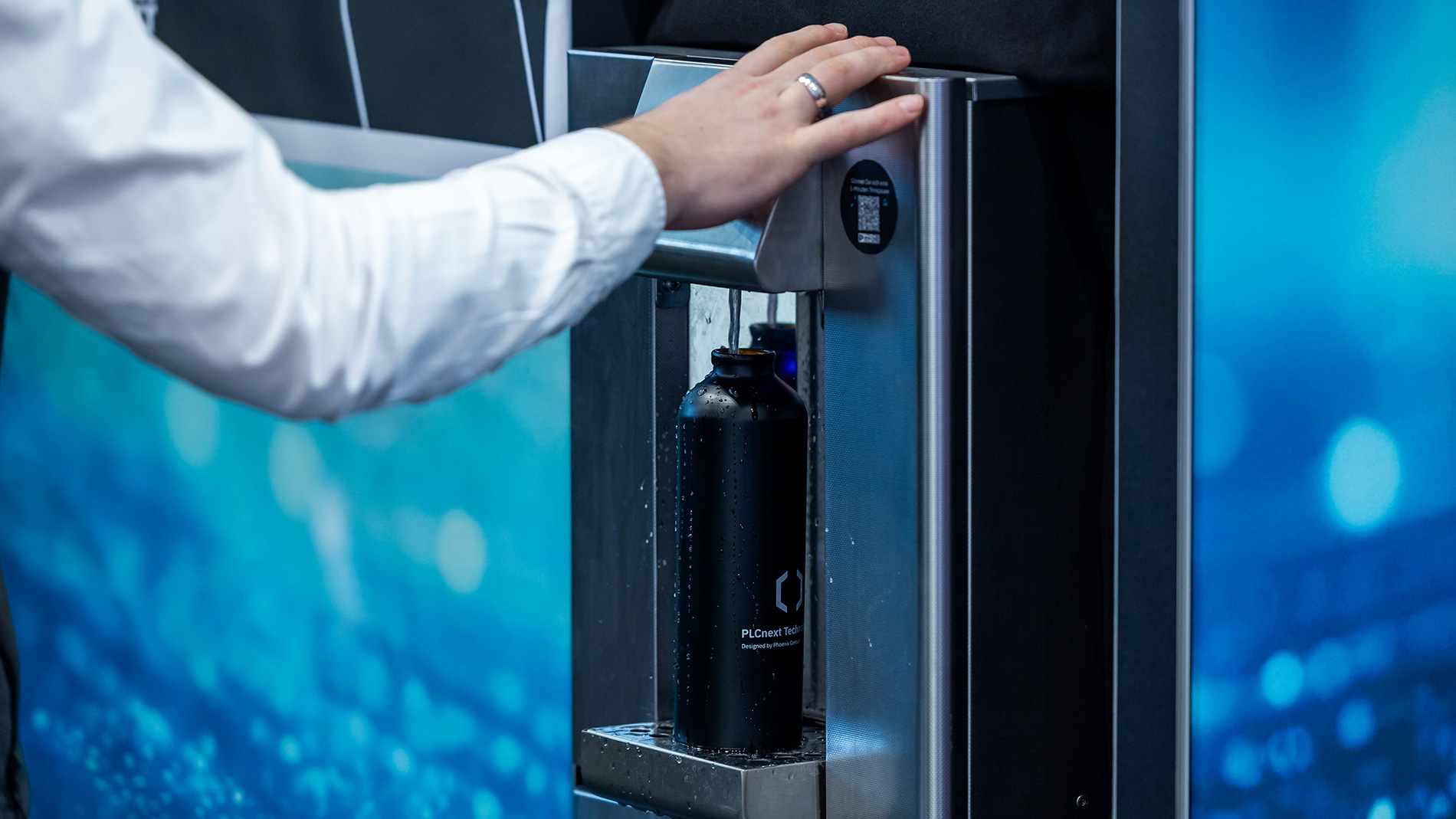 Besucher füllt eine wiederverwendbare Wasserflasche an einem Wasserspender auf dem Messegelände auf.