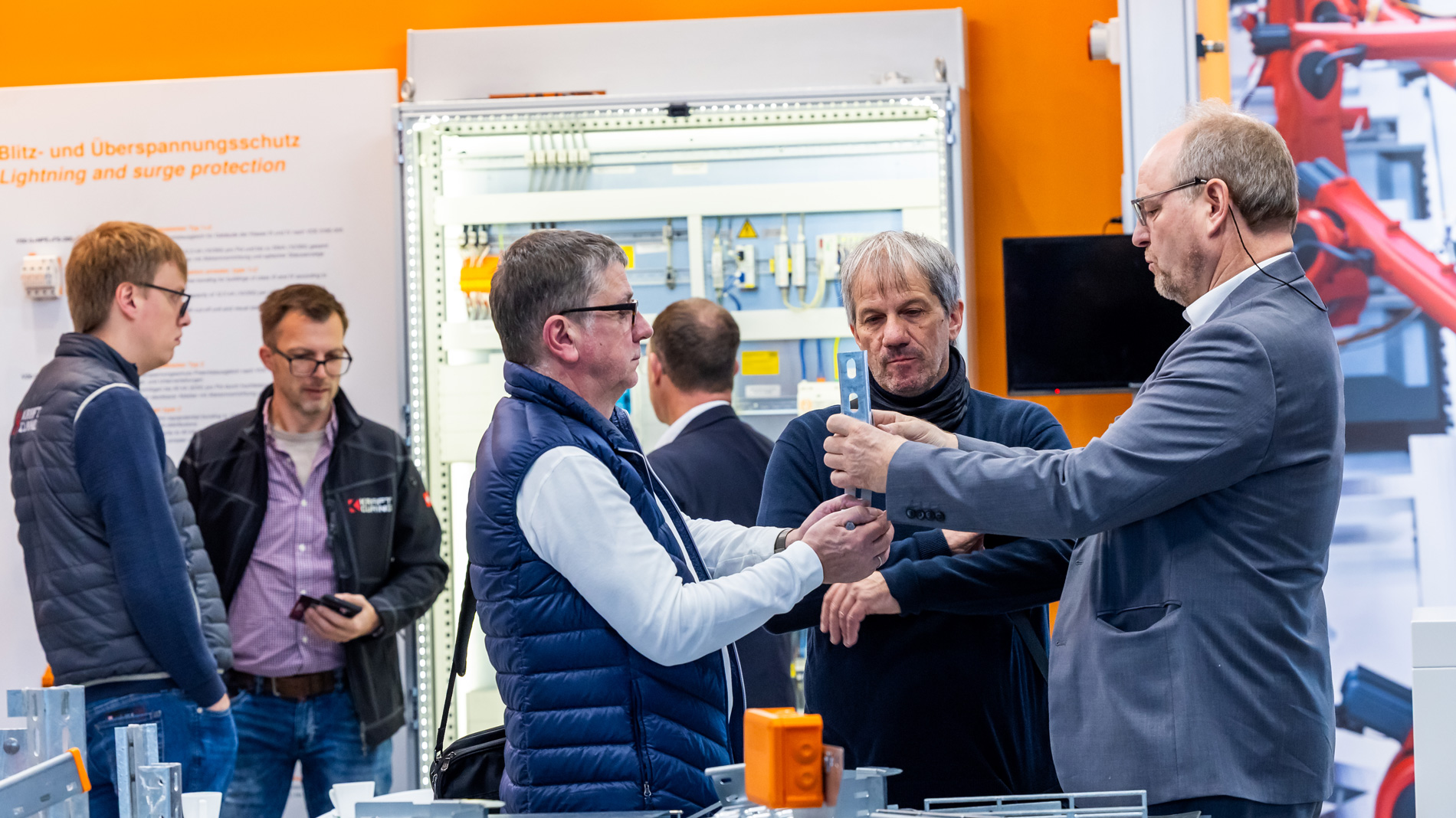 Mehrere Fachbesucher auf einer Industriemesse begutachten gemeinsam ein Bauteil an einem Messestand.